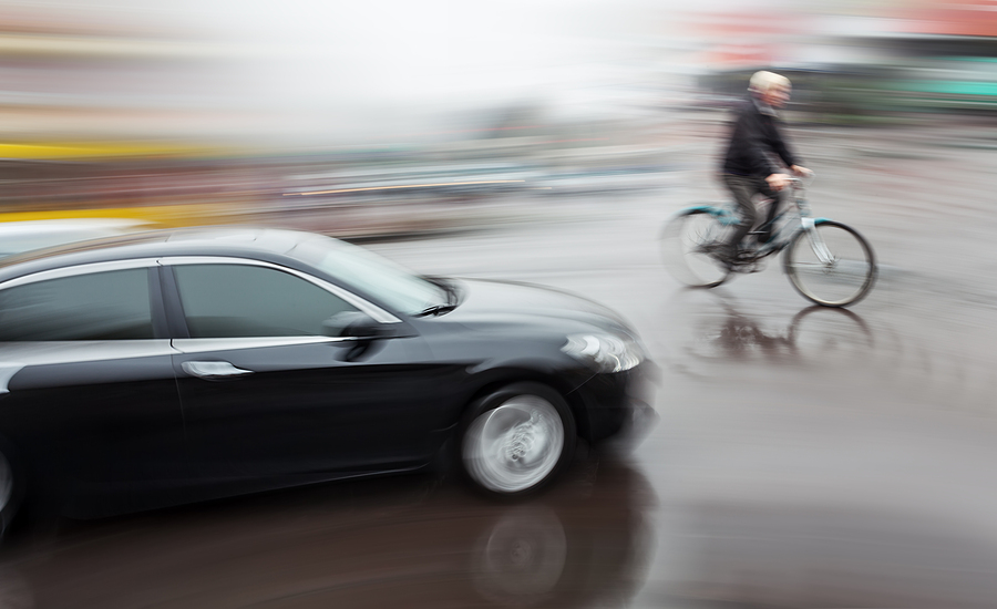 blurry bicyclist dangerously crosses in front of moving car