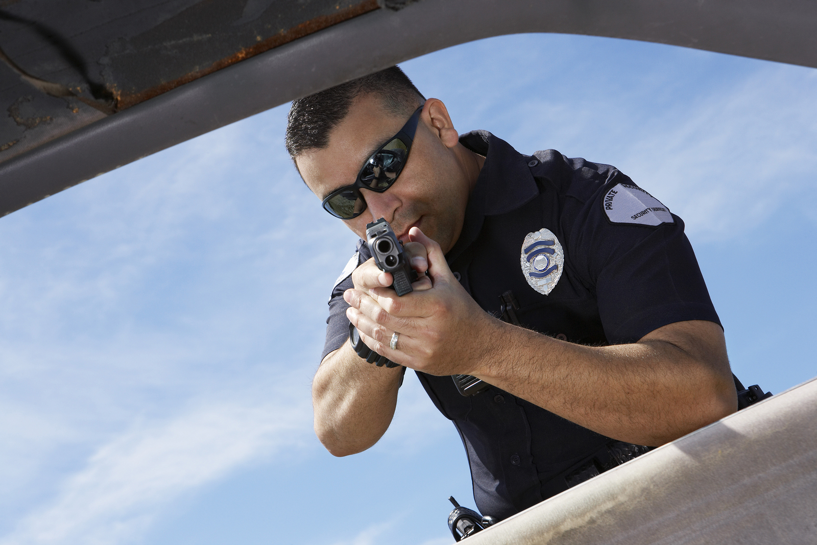 Male police officer aiming gun at broken car